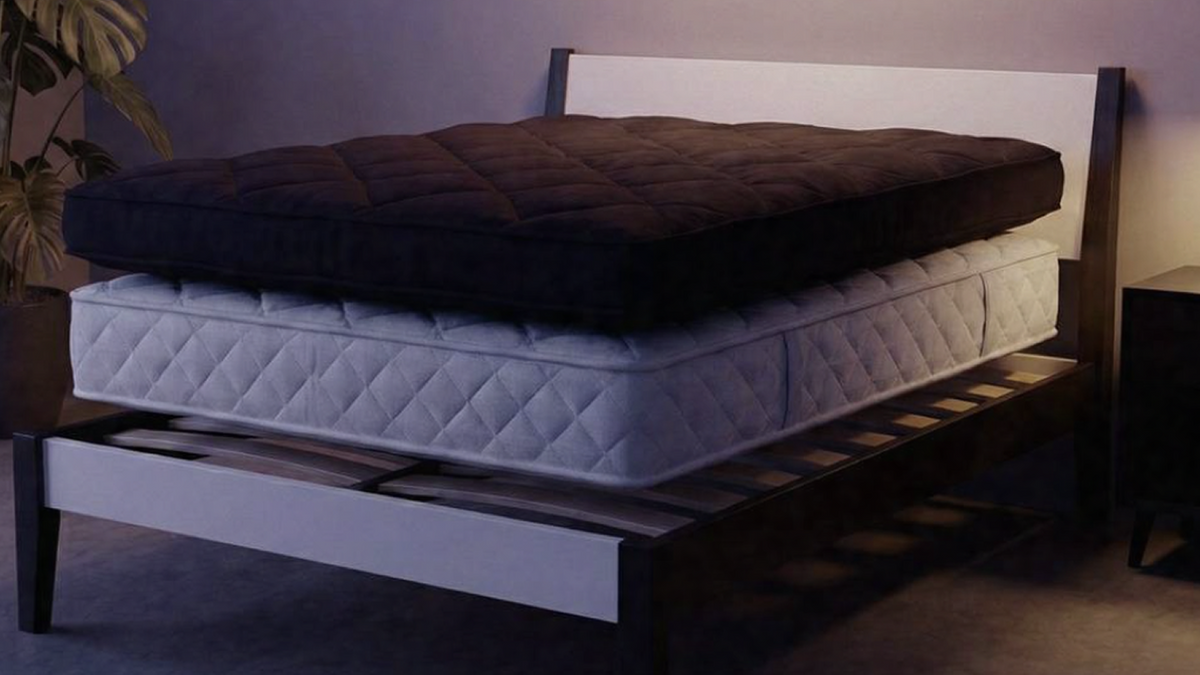 Dark quilted mattress topper lifted above a white quilted mattress on a wooden slatted bed frame, showing how the layers fit together